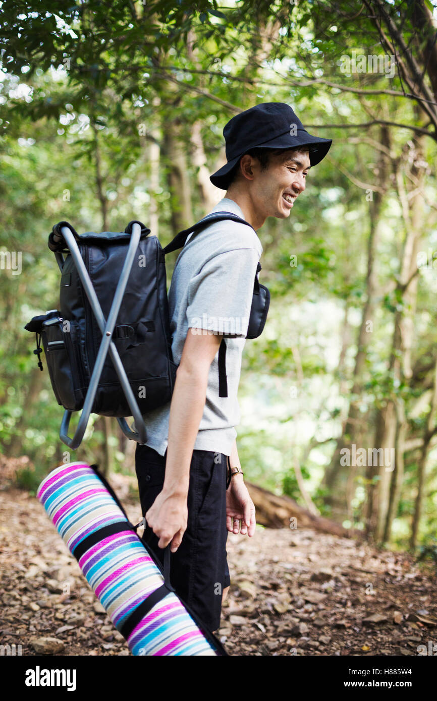 Mann in einem Wald steht, trägt eine Picknickdecke und Rucksack. Stockfoto