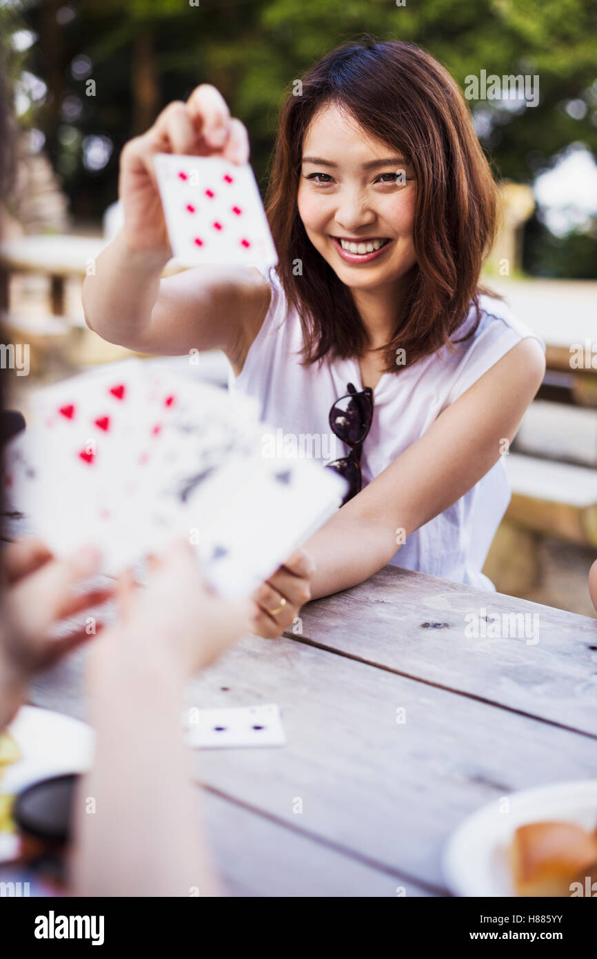 Lächelnde junge Frau sitzt an einem Tisch, Spielkarten. Stockfoto