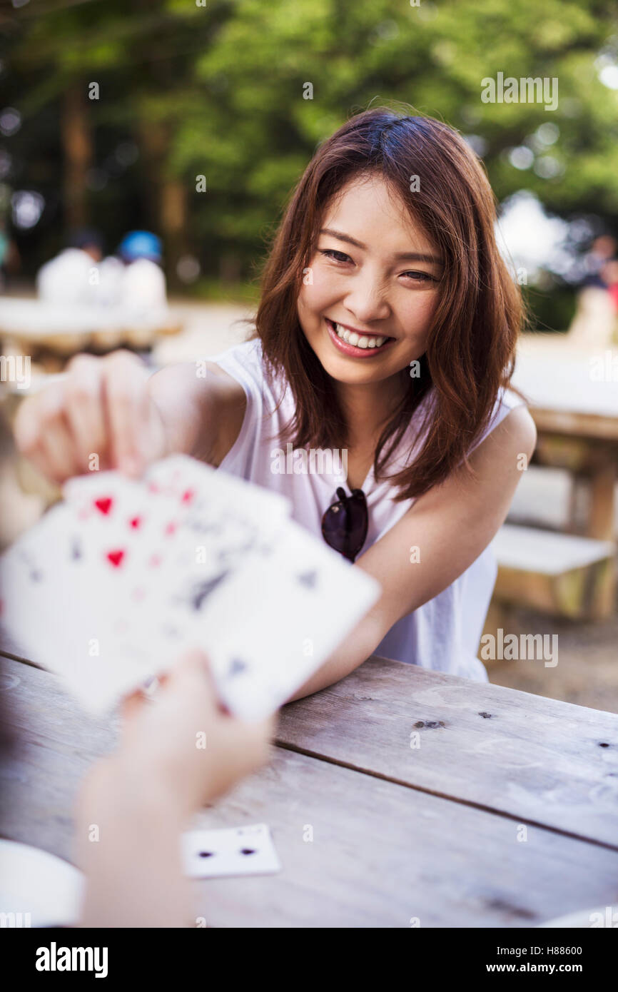 Lächelnde junge Frau sitzt an einem Tisch, Spielkarten. Stockfoto