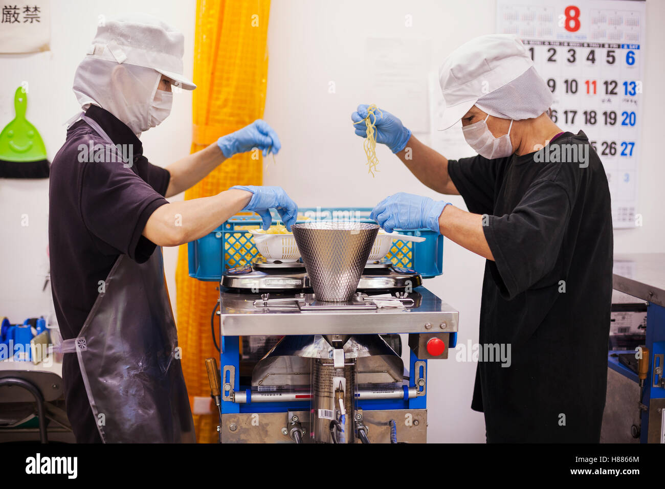 Arbeiter in Schürzen und Handschuhe, wiegen und Verpacken frisch Nudeln in einer Produktionseinheit Soba Nudeln gemacht. Stockfoto