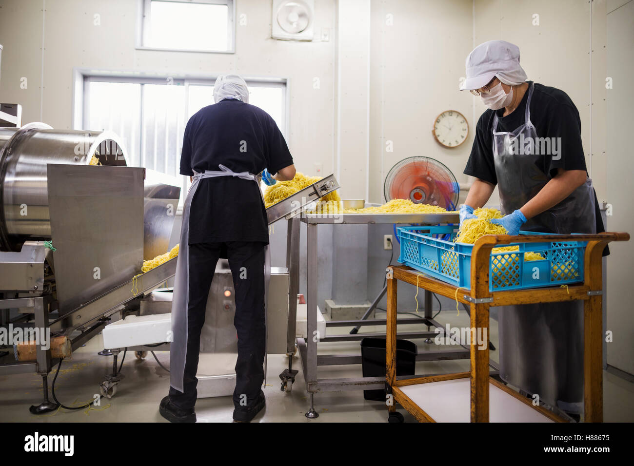 Arbeiter in Schürzen und Hüte sammeln frisch schneiden Nudeln vom Förderband zu verpacken und zu verkaufen. Stockfoto