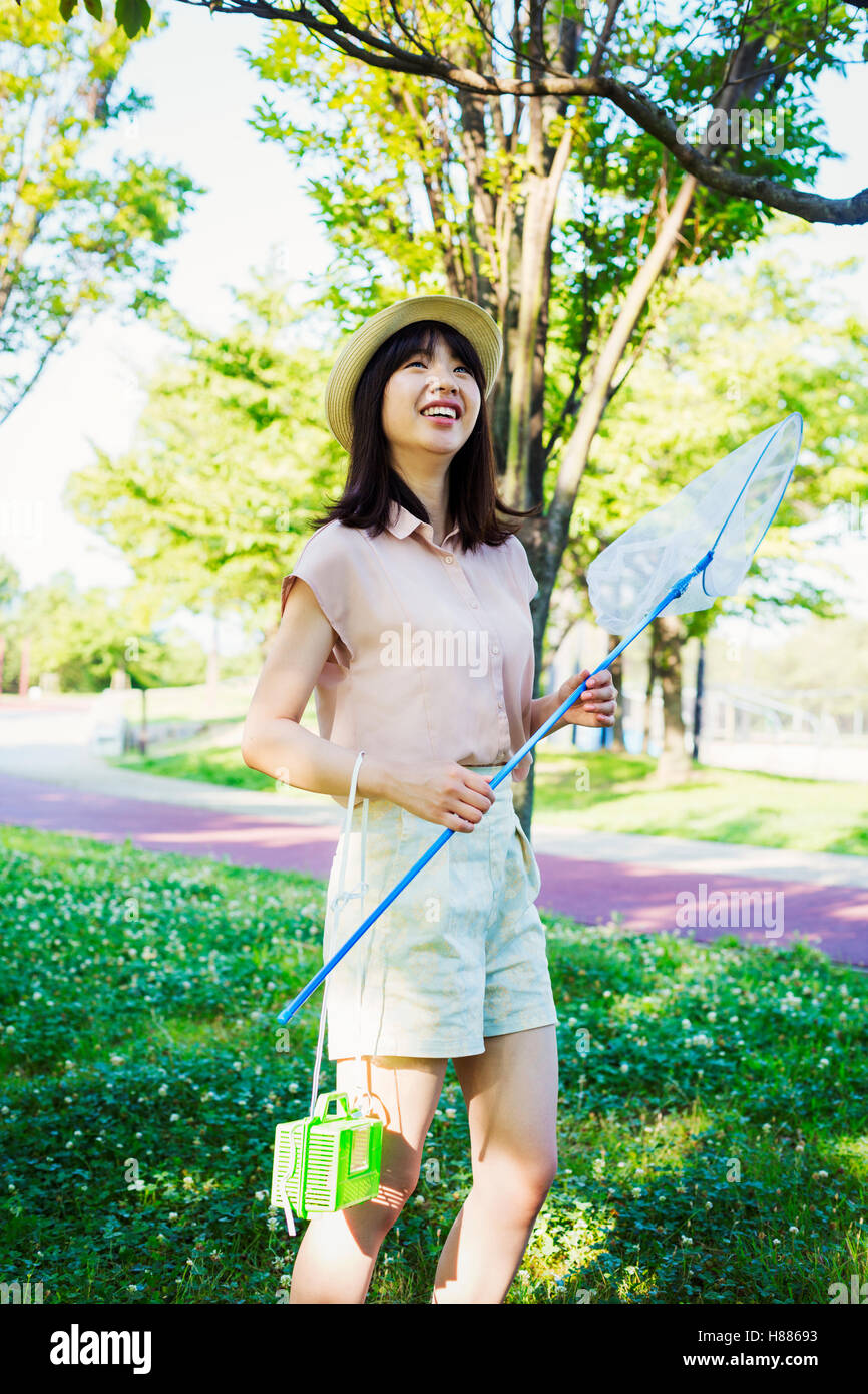 Junge Frau mit langen braunen Haaren steht in einem Park, hält ein Schmetterlingsnetz. Stockfoto