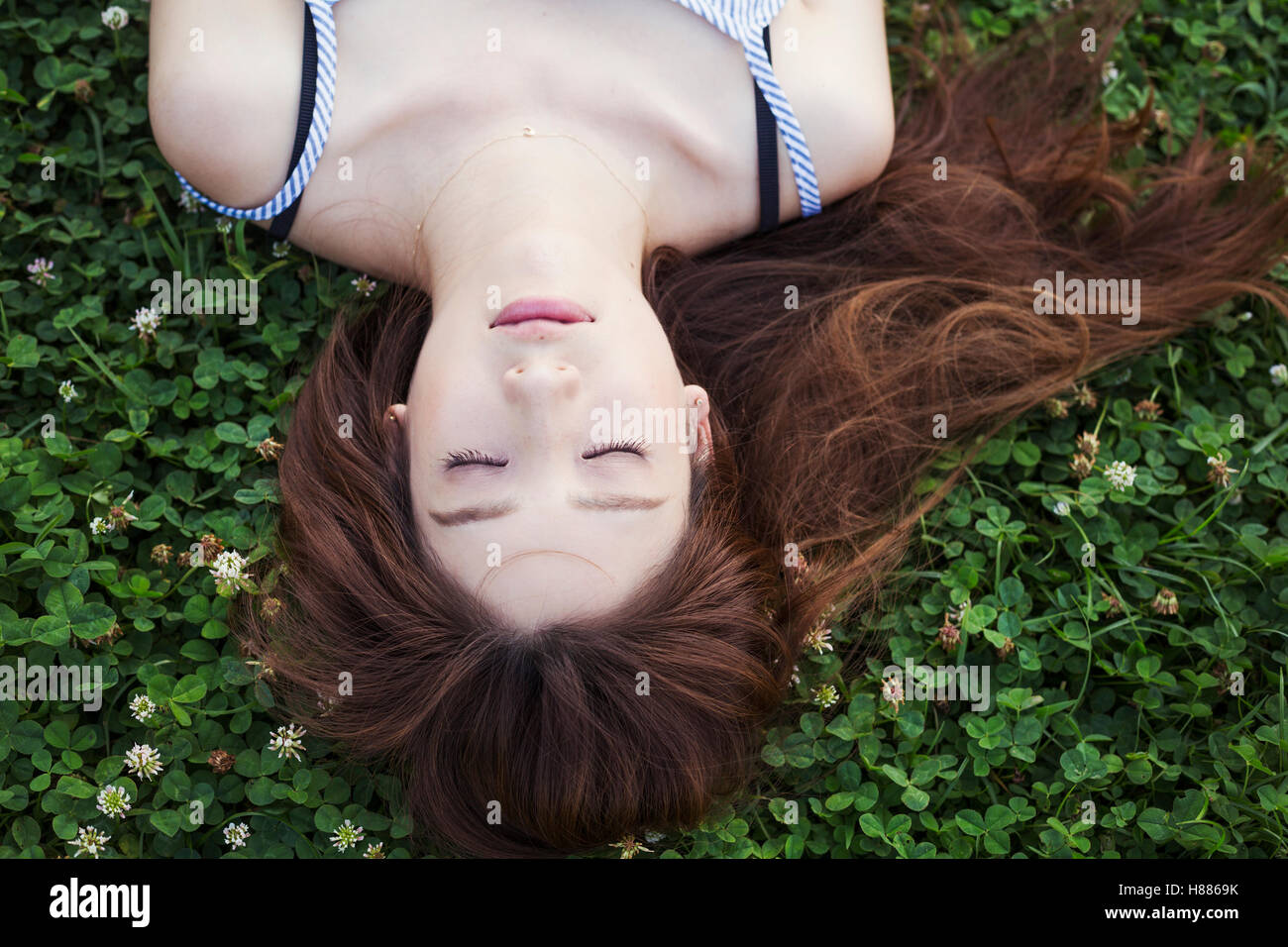 Junge Frau mit langen braunen Haaren, die auf einer Wiese liegen. Stockfoto