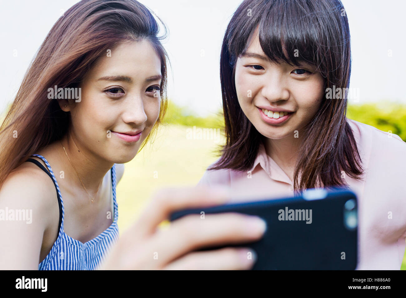 Zwei lächelnde junge Frauen mit langen braunen Haaren, hält ein Handy nehmen Selfie. Stockfoto