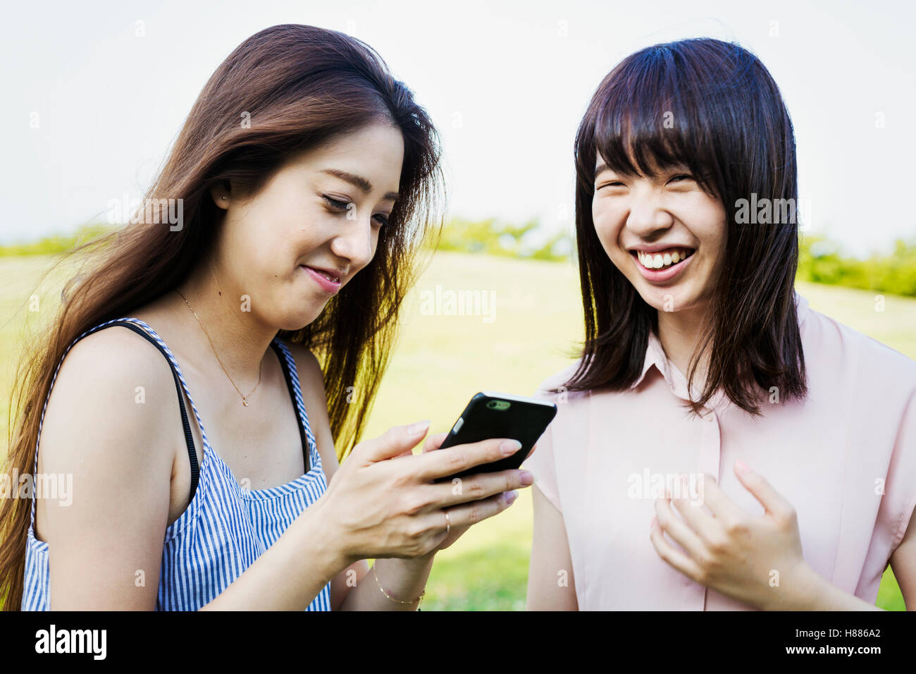 Zwei lächelnde junge Frauen mit langen braunen Haaren, halten eines Handys. Stockfoto