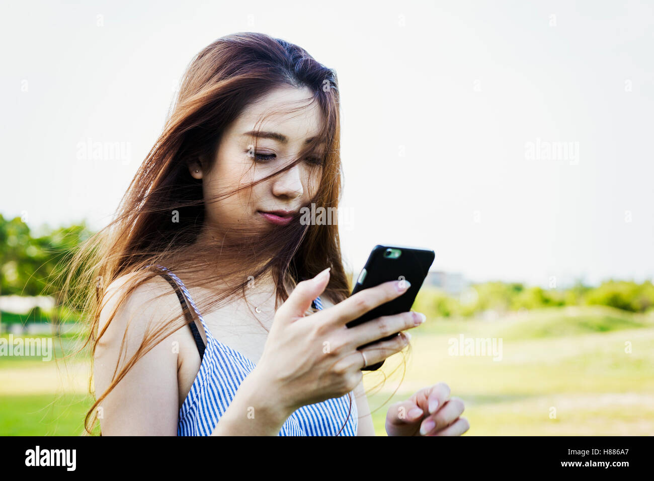 Lächelnde junge Frau mit langen braunen Haaren, halten eines Handys. Stockfoto