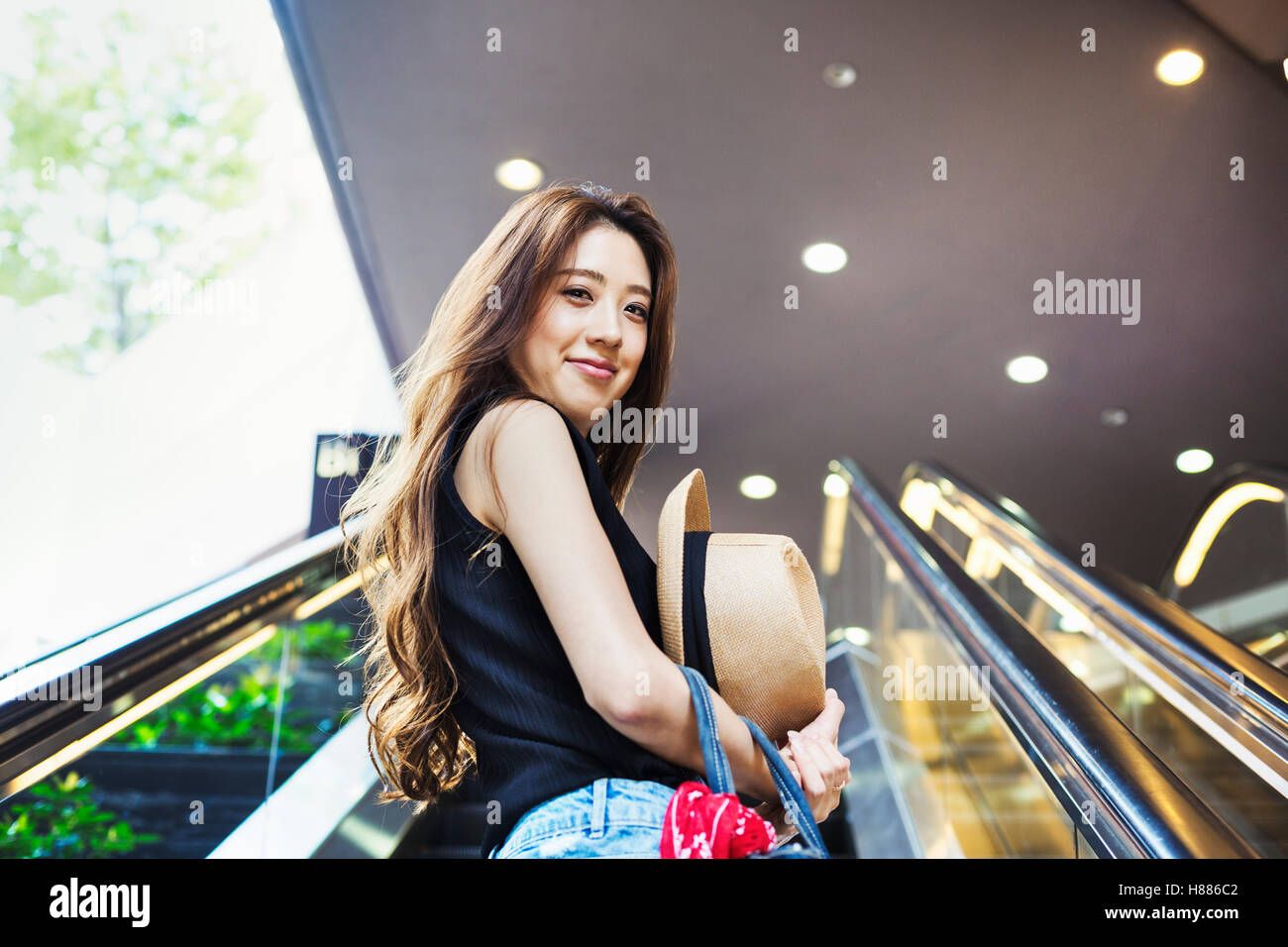 Lächelnde junge Frau mit langen braunen Haaren auf einer Rolltreppe. Stockfoto