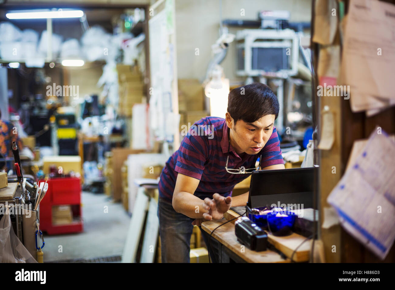 Ein Mann mit einem Laptopcomputer in ein Glas Hersteller Werkstatt. Stockfoto