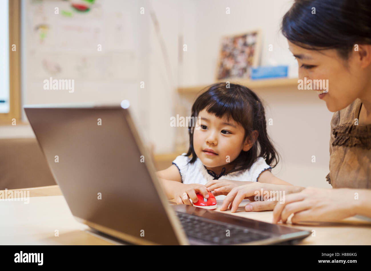 Haus der Familie. Eine Frau und ihre Tochter sitzen an einem Tisch, Blick auf dem Bildschirm eines Laptops. Stockfoto