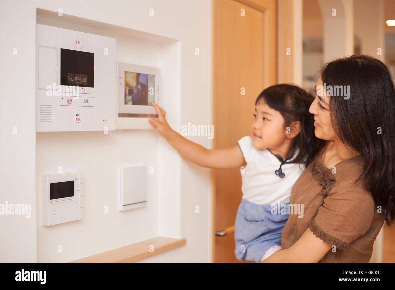 Haus der Familie. Eine Frau und ihre Tochter Blick auf einem Bildschirm an der Wand, Steuerelemente einer Türsprechanlage oder Tür. Stockfoto