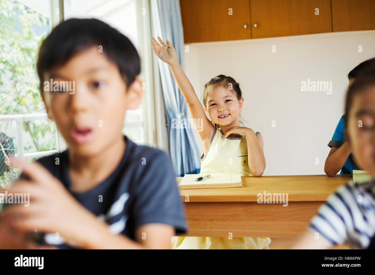 Eine Gruppe von Kindern in einem Klassenzimmer, einem mit der Hand bereit, eine Frage zu beantworten. Stockfoto