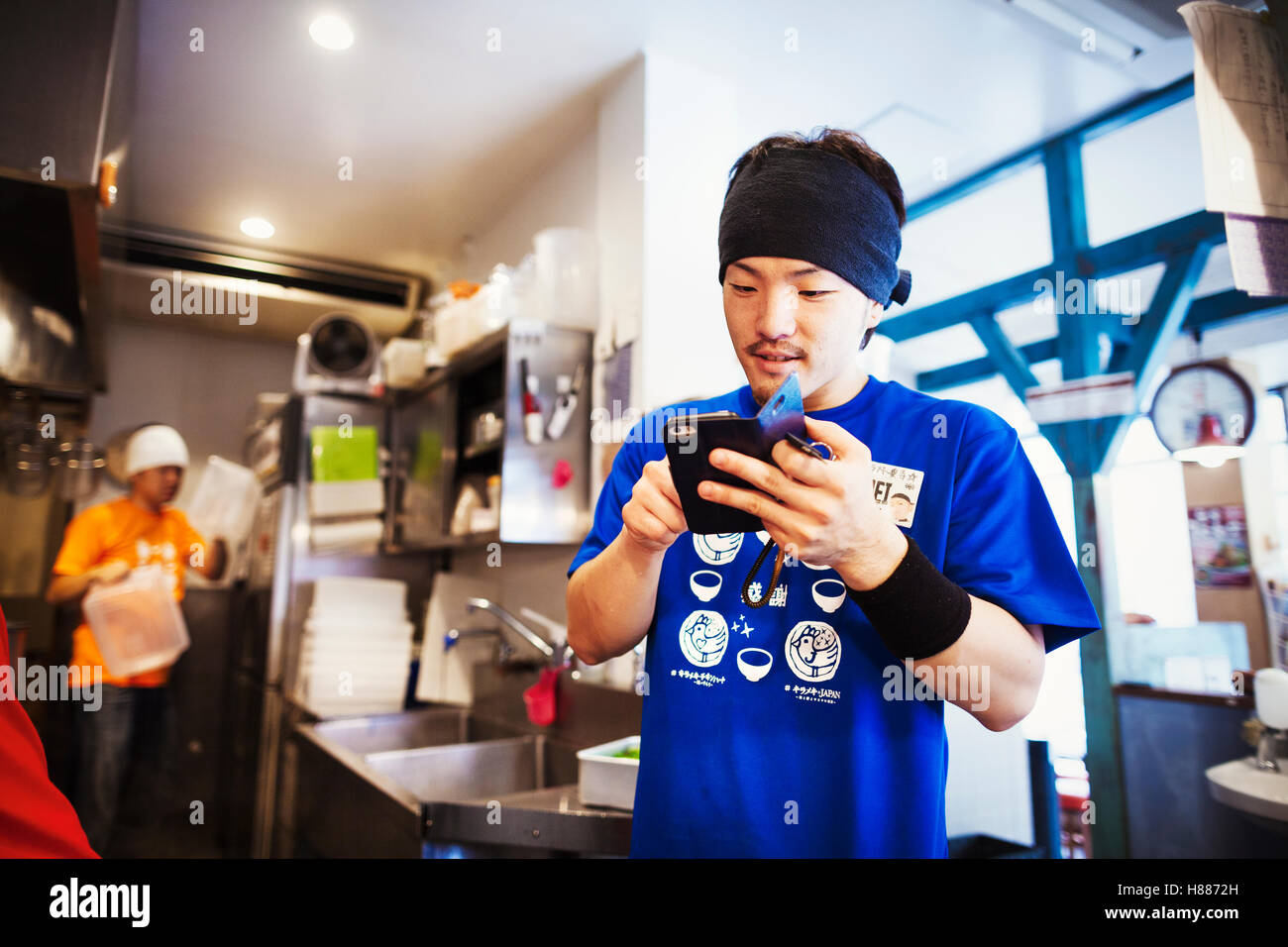 Die Ramen-Nudel-Shop, Personal, die Zubereitung von Speisen. Ein Koch mit einem Smartphone in einer Küche. Stockfoto