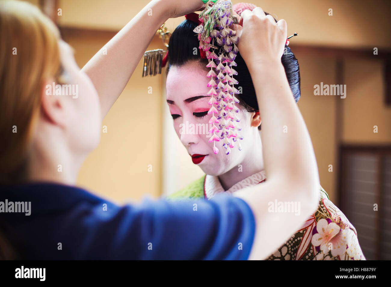 Eine Geisha und Maiko mit Friseur- und Make-up-Künstler. Eine aufwendige Blumendekoration mit langen Fransen im Haar fixiert. Stockfoto