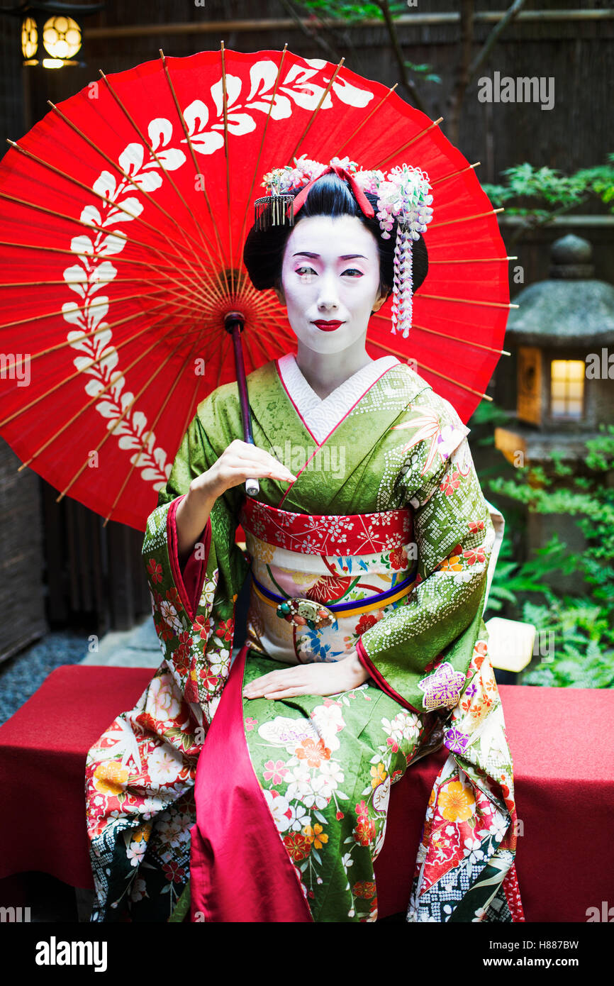 Eine Frau in die traditionelle Geisha-Stil gekleidet, trägt einen Kimono und Obi, sitzen mit einem Regenschirm. Stockfoto