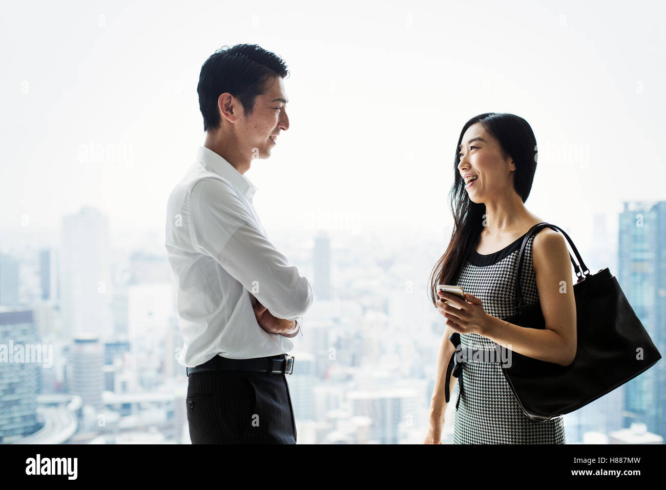 Ein Geschäftsmann und Geschäftsfrau stehend reden durch ein großes Fenster mit Blick auf eine Stadt Stockfoto