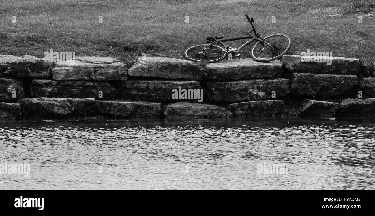 altes Fahrrad links auf der steinernen Bank des Flusses mit Grünstreifen Stockfoto