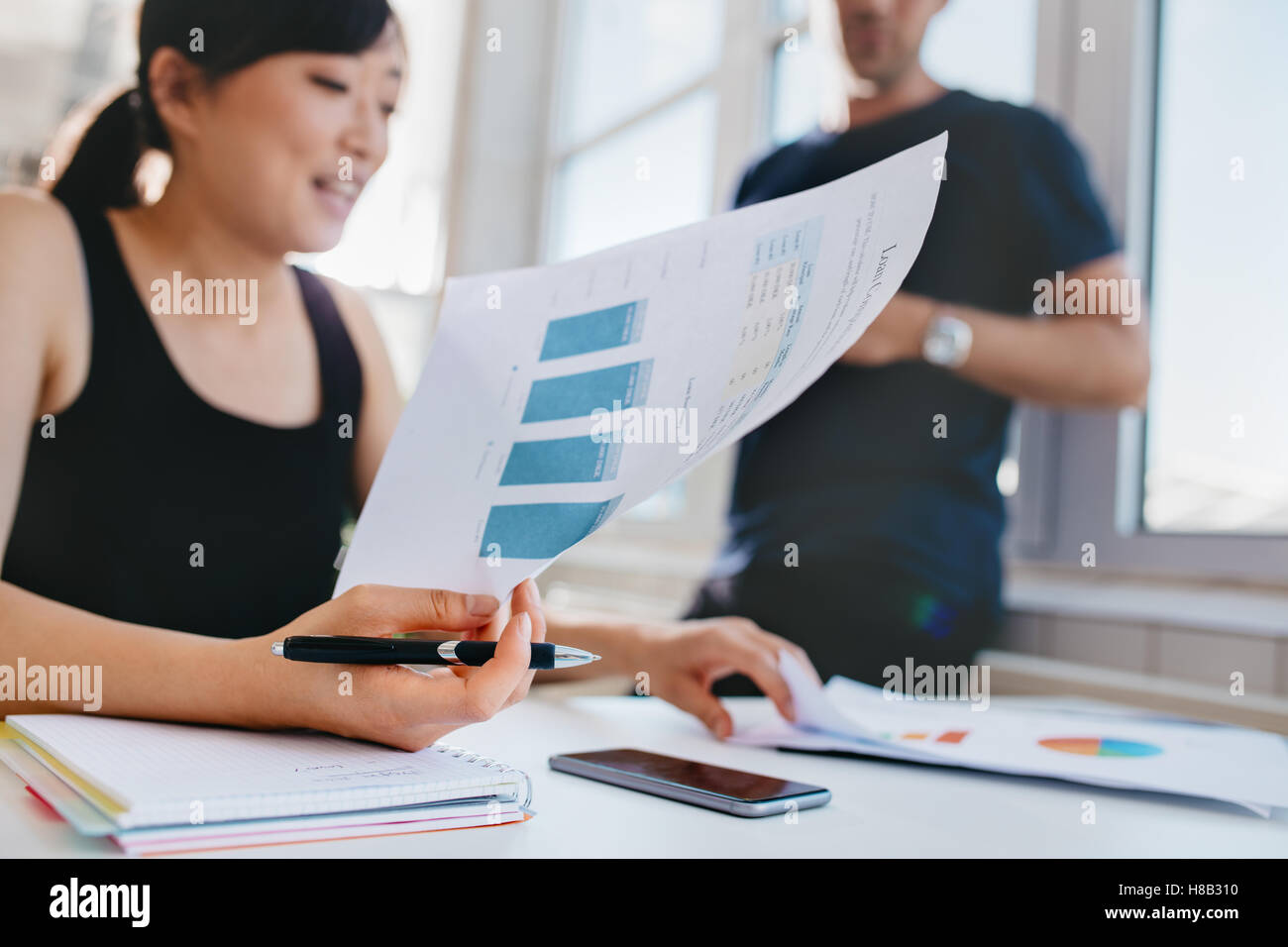 Frau mit männlicher Kollege im Hintergrund stehen Finanzanalyse im Büro zu tun. Asiatische Frauen halten Dokumente beim sittin Stockfoto