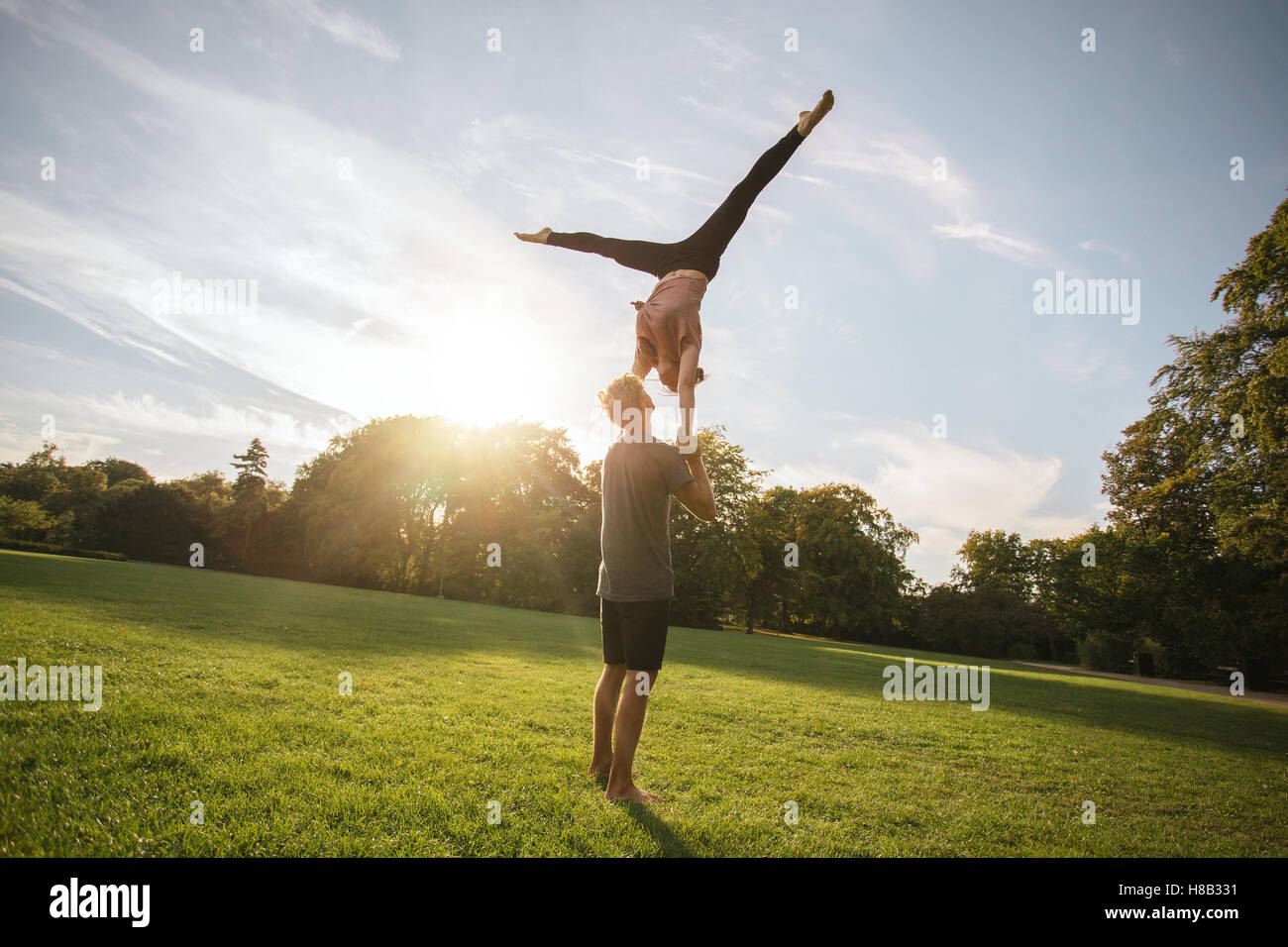 Passen Sie junges Paar beim Acro Yoga im Park. Mann hält und den Ausgleich von Frau in der Luft. Stockfoto