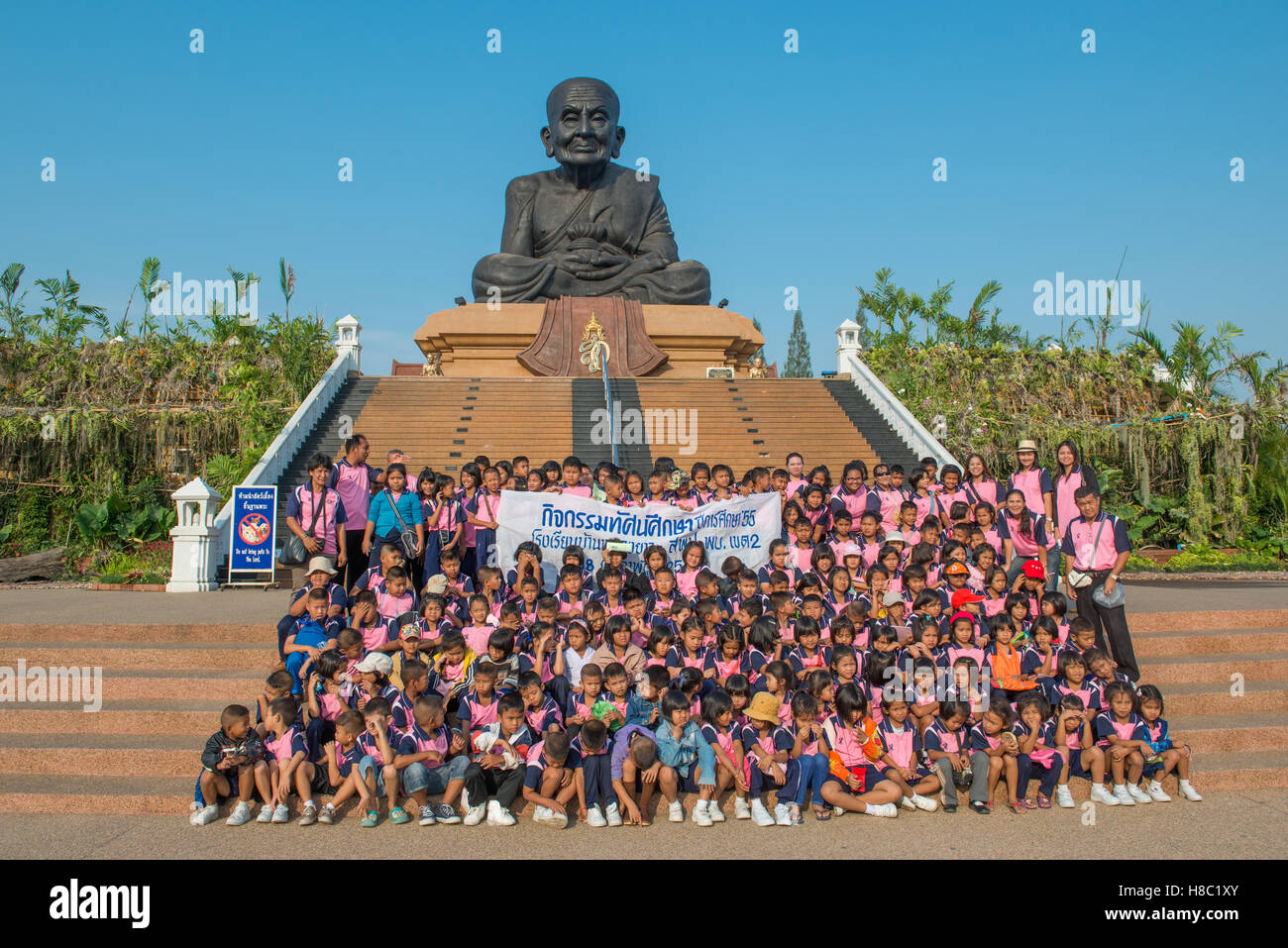 Thailändische Schulkinder mit einem Gruppenfoto vor der berühmten Skulptur verehrten buddhistischen Mönchs Luang Pu Thuat Wat Huay m Stockfoto