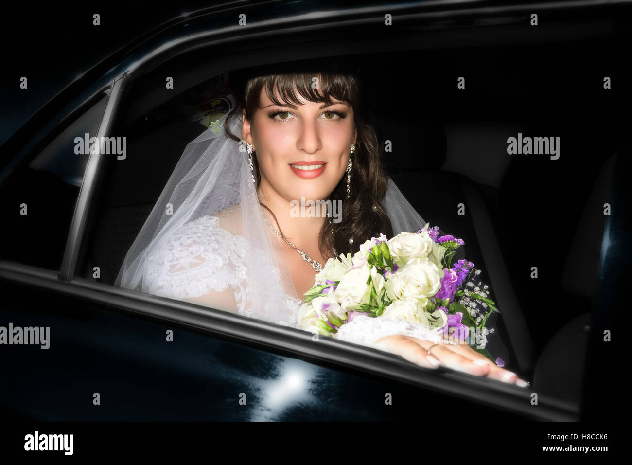 Schöne lächelnde Braut mit einem Brautstrauß in Autofenster Stockfoto