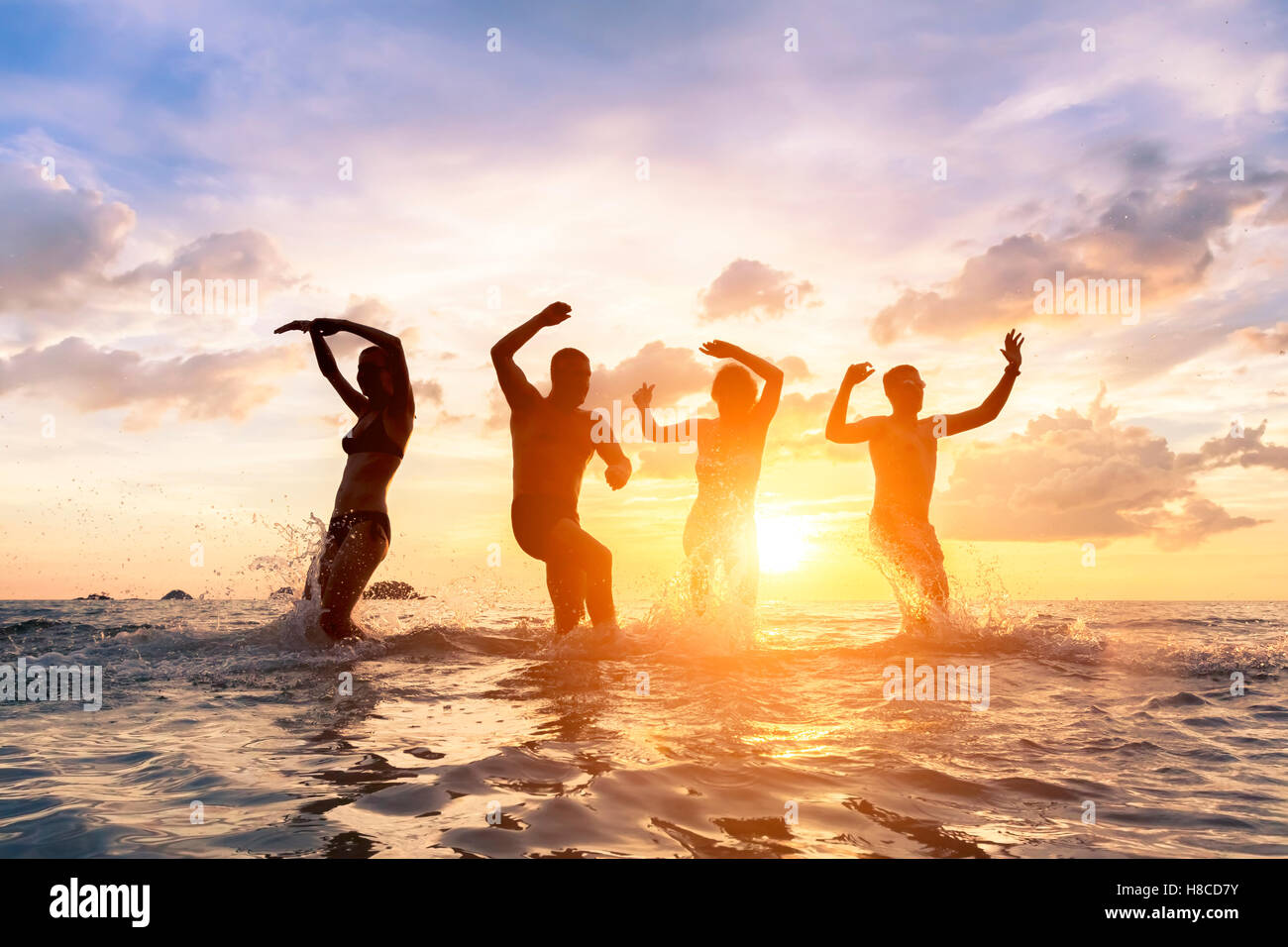 Gruppe von jungen Leuten Spaß tanzen fröhlich glücklich Freunde im Meer mit Spritzwasser, Stockfoto