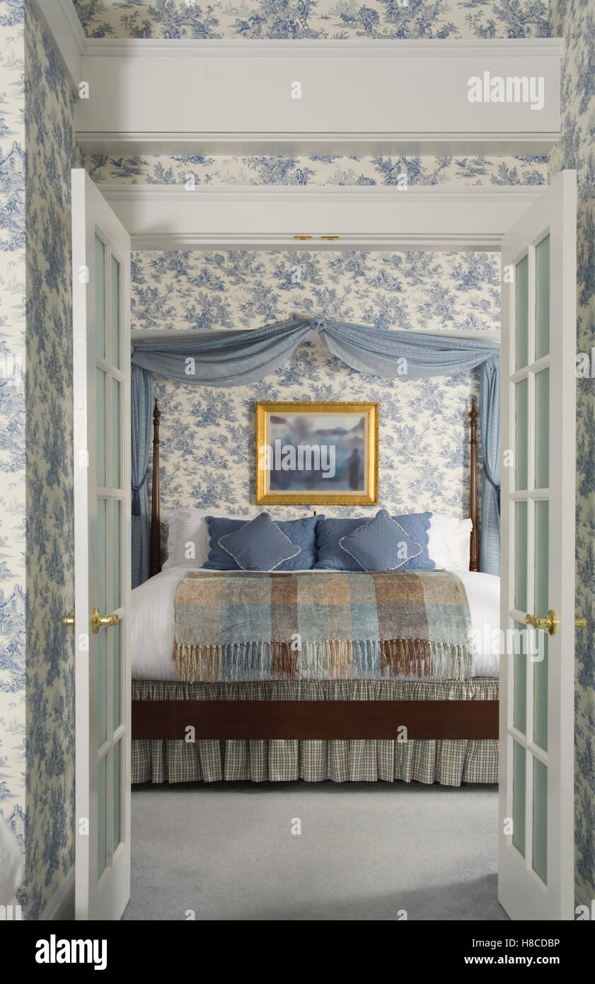 Blick durch offene Doppeltüren mit blauen Vorhängen oben ins Bett. Stockfoto