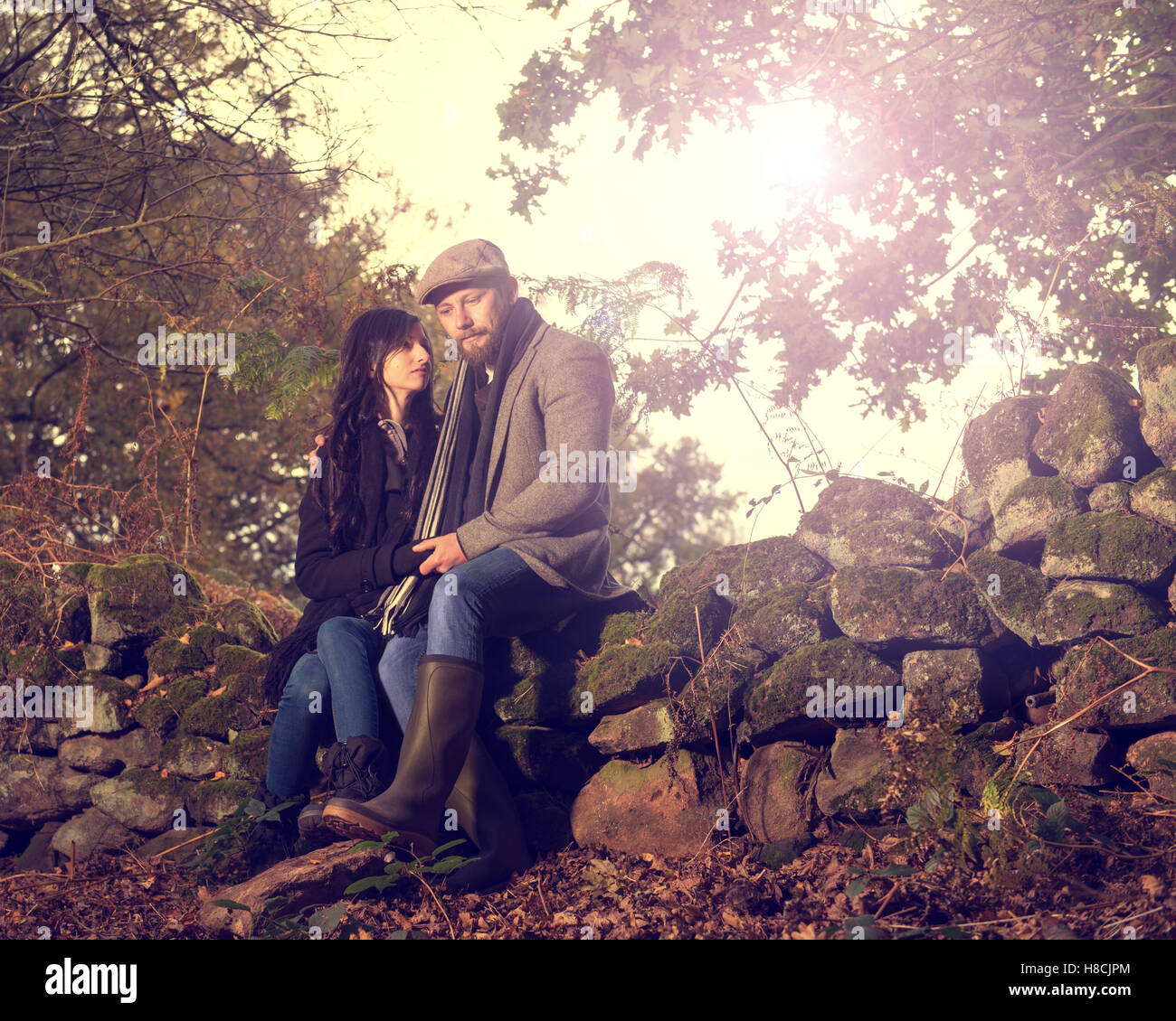 Young 30 Paar sitzt auf Stein Wand im Herbst Einstellung Stockfoto