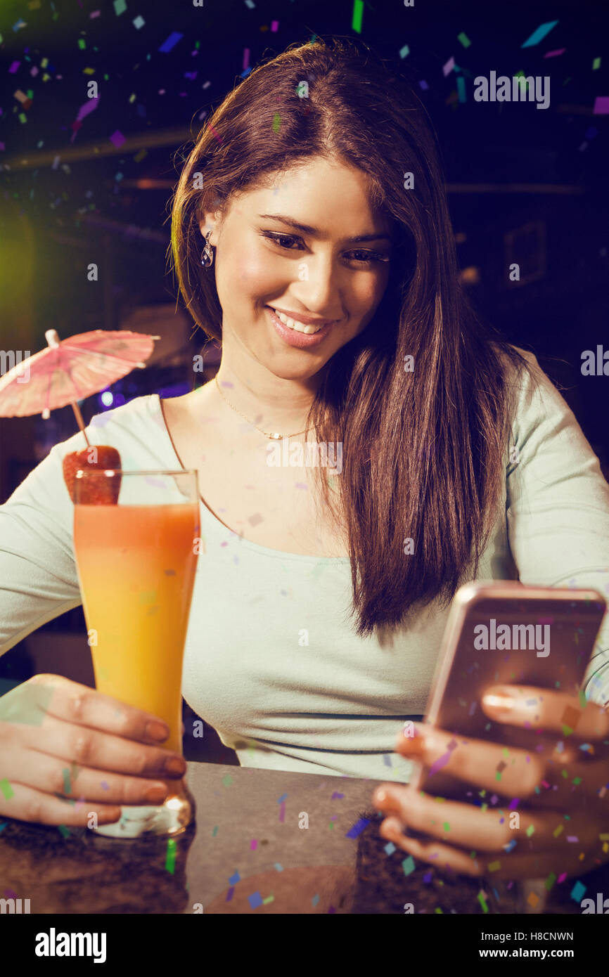 Zusammengesetztes Bild der schönen Frau Textmitteilung zu schreiben, während mit cocktail Stockfoto