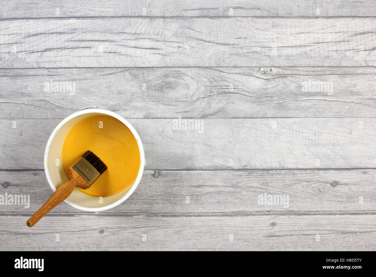 Pinsel, sitzt in einem weißen Anstrich Kessel gefüllt mit gelber Farbe auf einen Holzfußboden shabby Stil Stockfoto