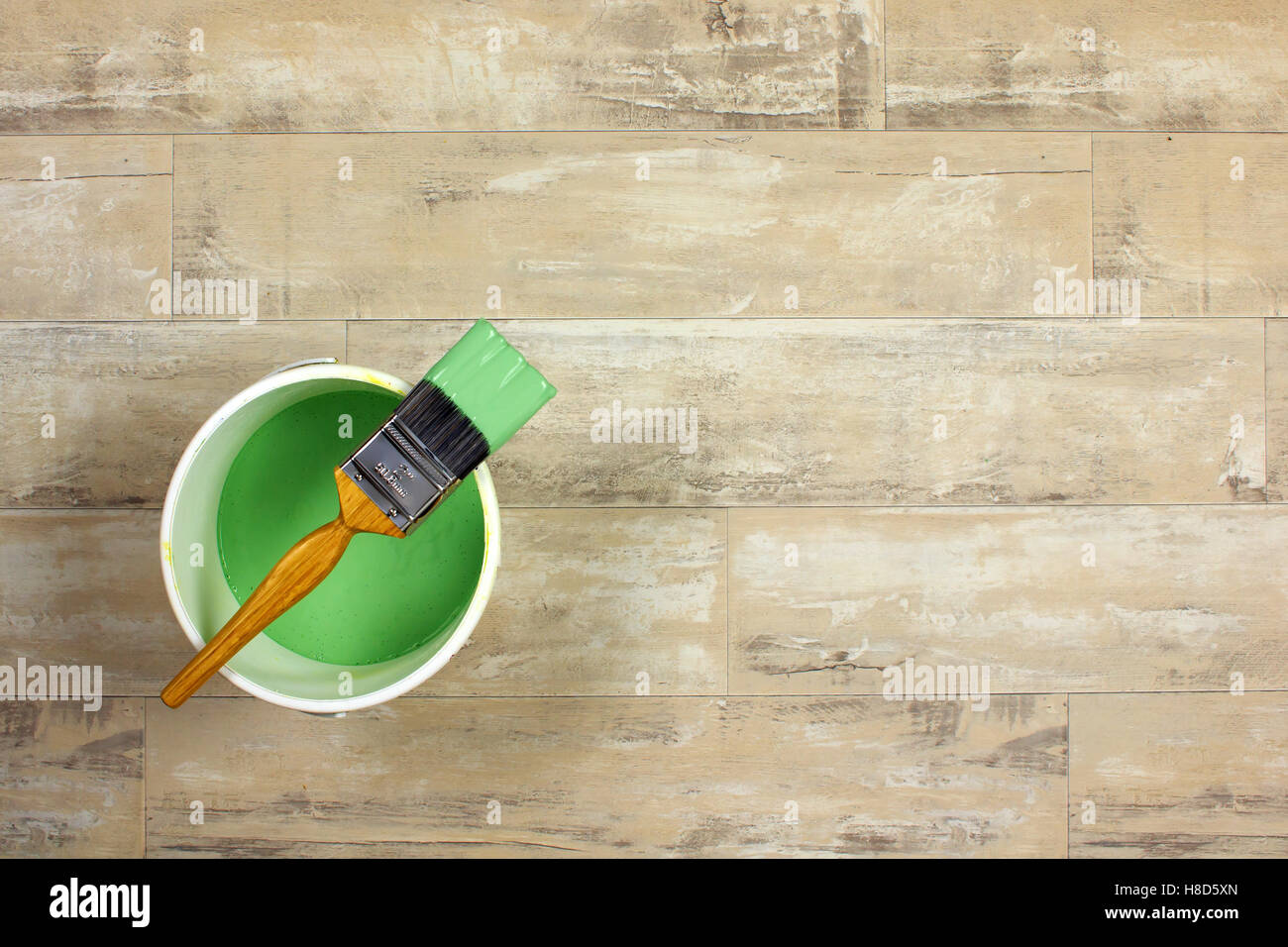 Geladenen Pinsel über eine weiße Farbe Wasserkocher gelegt gefüllt mit grüner Farbe auf einen Holzfußboden shabby Stil Stockfoto