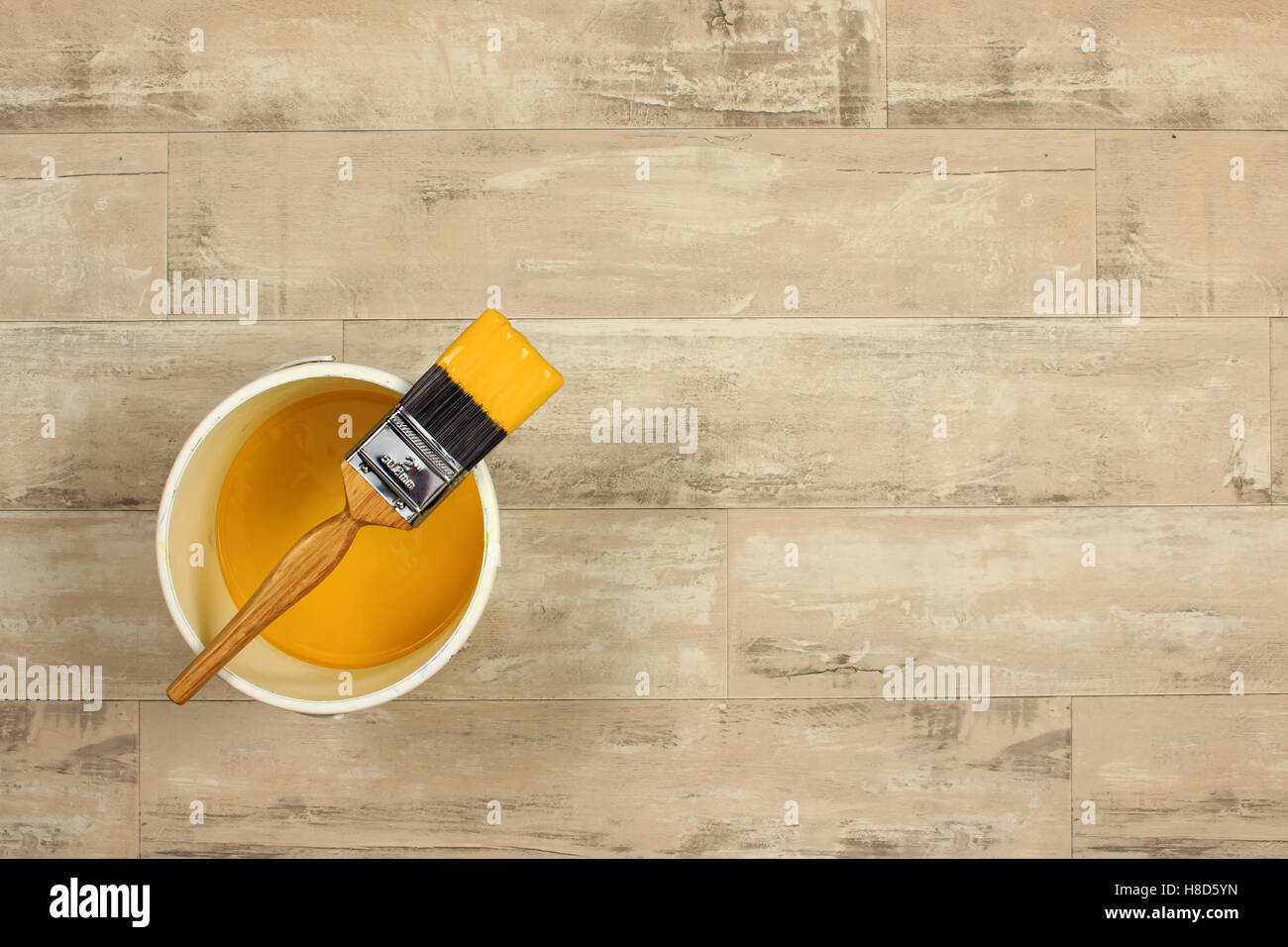 geladenen Pinsel über eine weiße Farbe Wasserkocher gelegt gefüllt mit gelber Farbe auf einen Holzfußboden shabby Stil Stockfoto