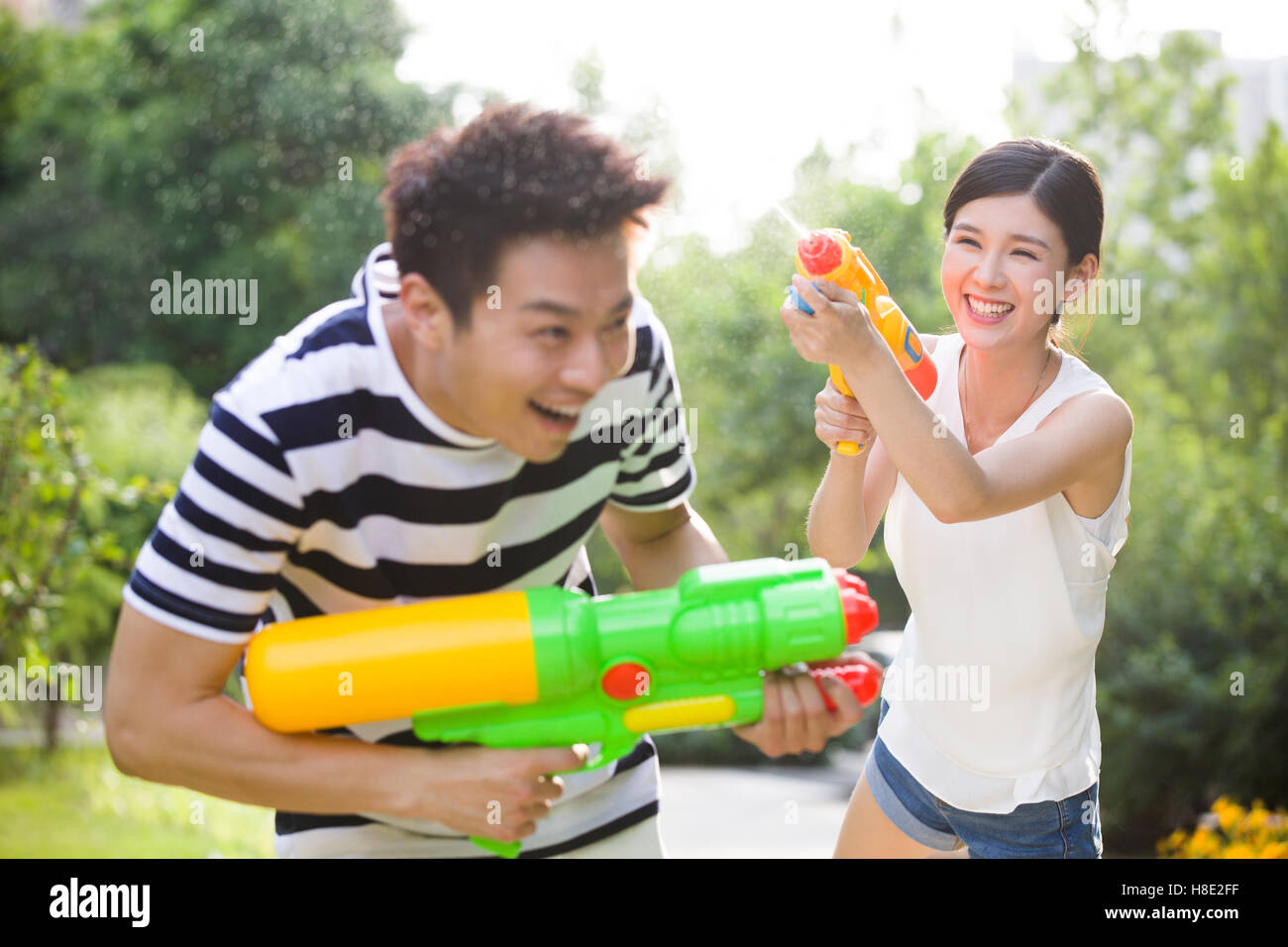 Glückliche junge chinesische paar spielen Spritzpistolen Stockfoto