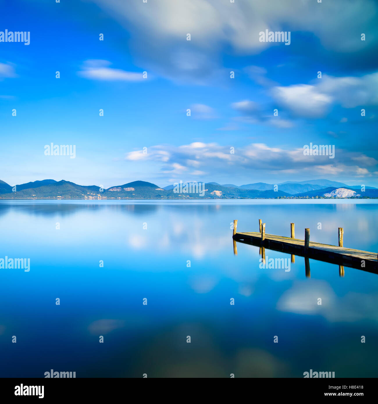 Hölzerne Pier oder Steg und blauen See Sonnenuntergang und Himmel Reflexion auf dem Wasser. Langzeitbelichtung, Versilia Massaciuccoli See, Italien Stockfoto