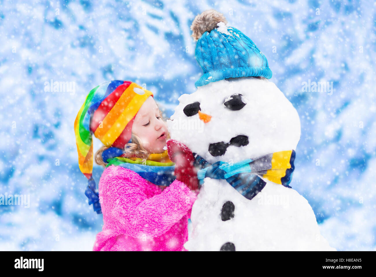 Lustige kleine Kleinkind Mädchen in eine bunte Mütze und warmen Mantel mit einem Schneemann spielen. Kinder spielen im Freien im Winter. C Stockfoto