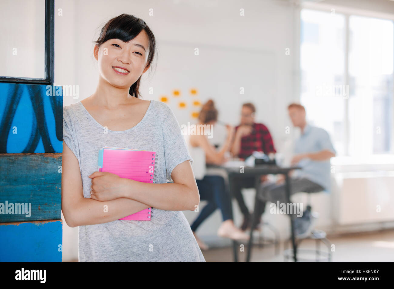 Porträt der lächelnde junge asiatische Frau im Büro mit Kollegen, die im Hintergrund stehen. Weibliche executive stehend mit h Stockfoto