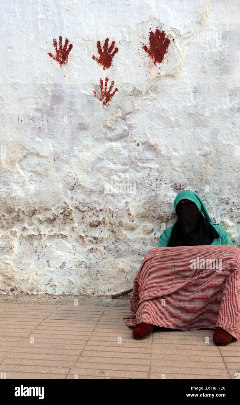 Eine verschleierte Frau sitzen durch eine bunte Wand in der alten Stadt-of-Sale in der Nähe von Rabat, Marokko. Stockfoto