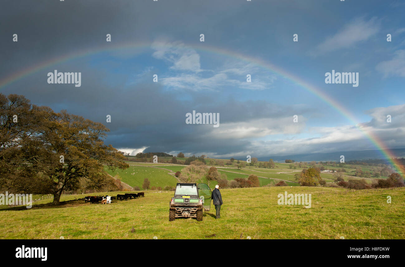 Bauer stand im Feld bewundern einen Regenbogen über Eden Valley, Cumbria, England. Stockfoto