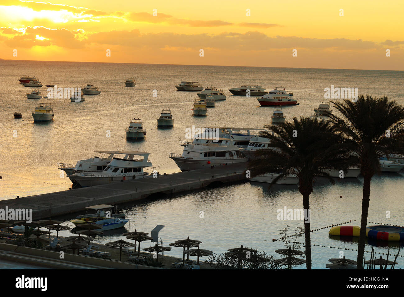 Yachten und Privatstrand mit Sonnenschirmen und lounging Stühle in einem Resort am Roten Meer in Hurghada, Ägypten bei Sonnenuntergang Stockfoto