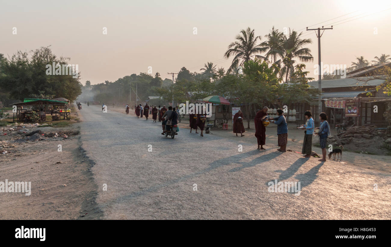 Straße Szene in ländlichen Myanmar in den frühen Morgenstunden. Mönchen Almosen von weiblichen Dorfbewohner erhalten. Shwe Kyet noch Dorf, Myanmar. Stockfoto