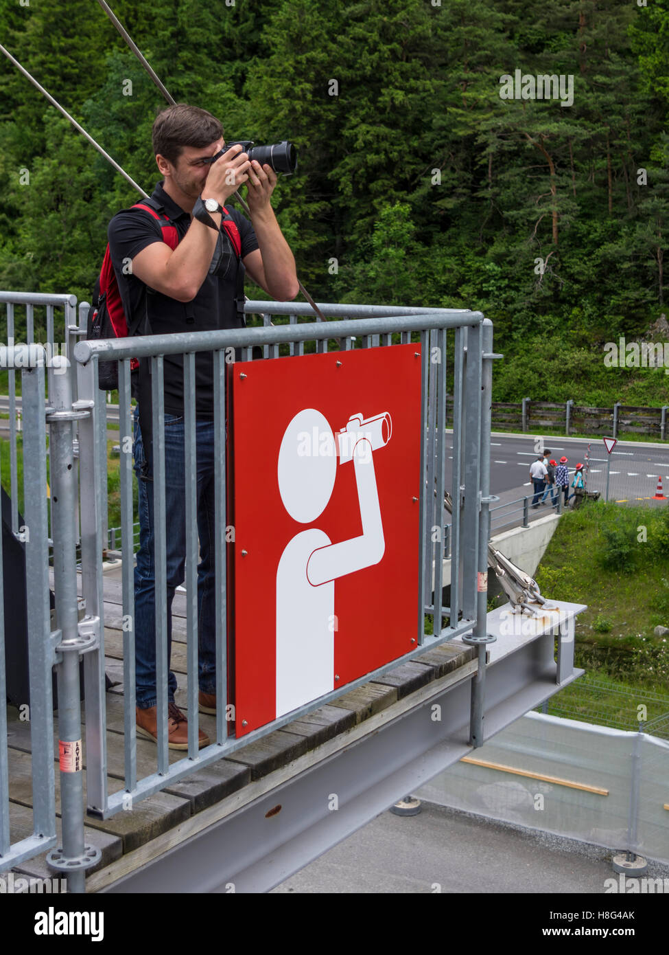 Junge Kaukasischen Männchen eine Aufnahme mit seiner Kamera von einem Aussichtspunkt mit einem großen Blickwinkel-Schild gekennzeichnet. Kanton Uri, Schweiz. Stockfoto
