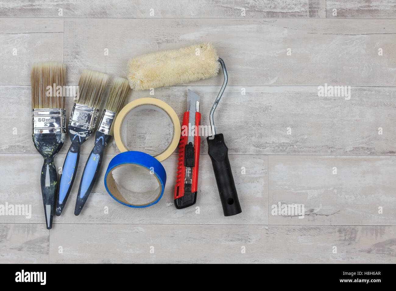 Malen Sie, Pinsel, Farbroller, Messer und Klebeband auf eine shabby Stil Holz Boden Stockfoto