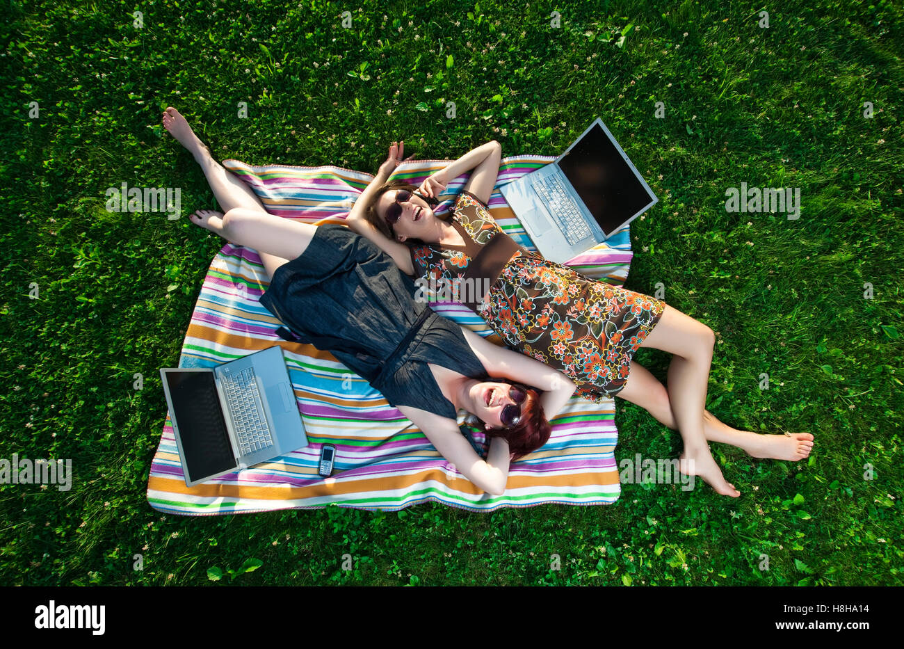Zwei junge Frauen mit Laptop und Handy-Verlegung auf einer Decke in der Wiese Stockfoto