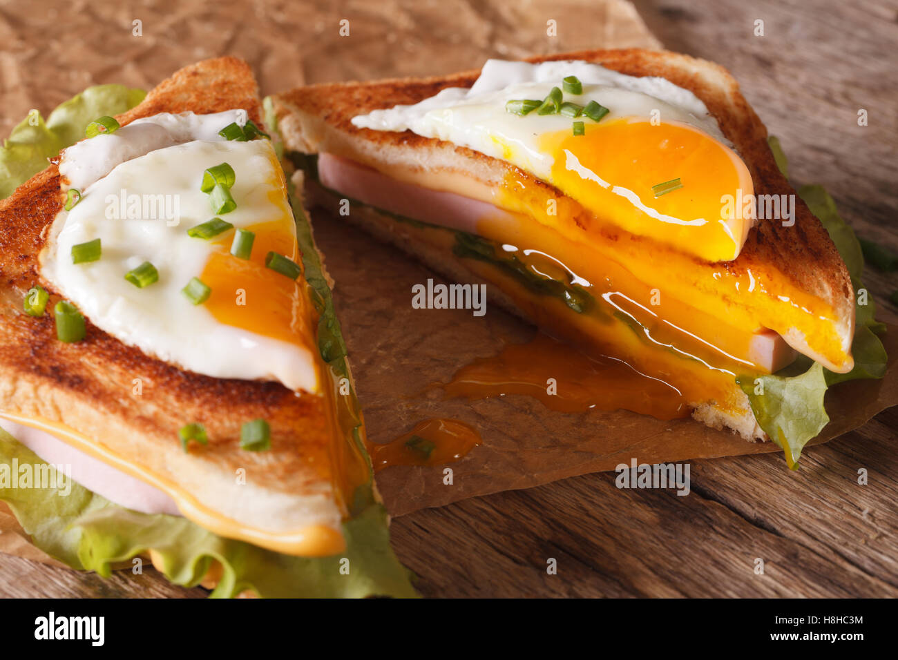 Schneiden Sie in einem halben Sandwich mit gebratenem Ei, Schinken und Käse Nahaufnahme auf dem Papier auf dem Tisch. horizontale Stockfoto