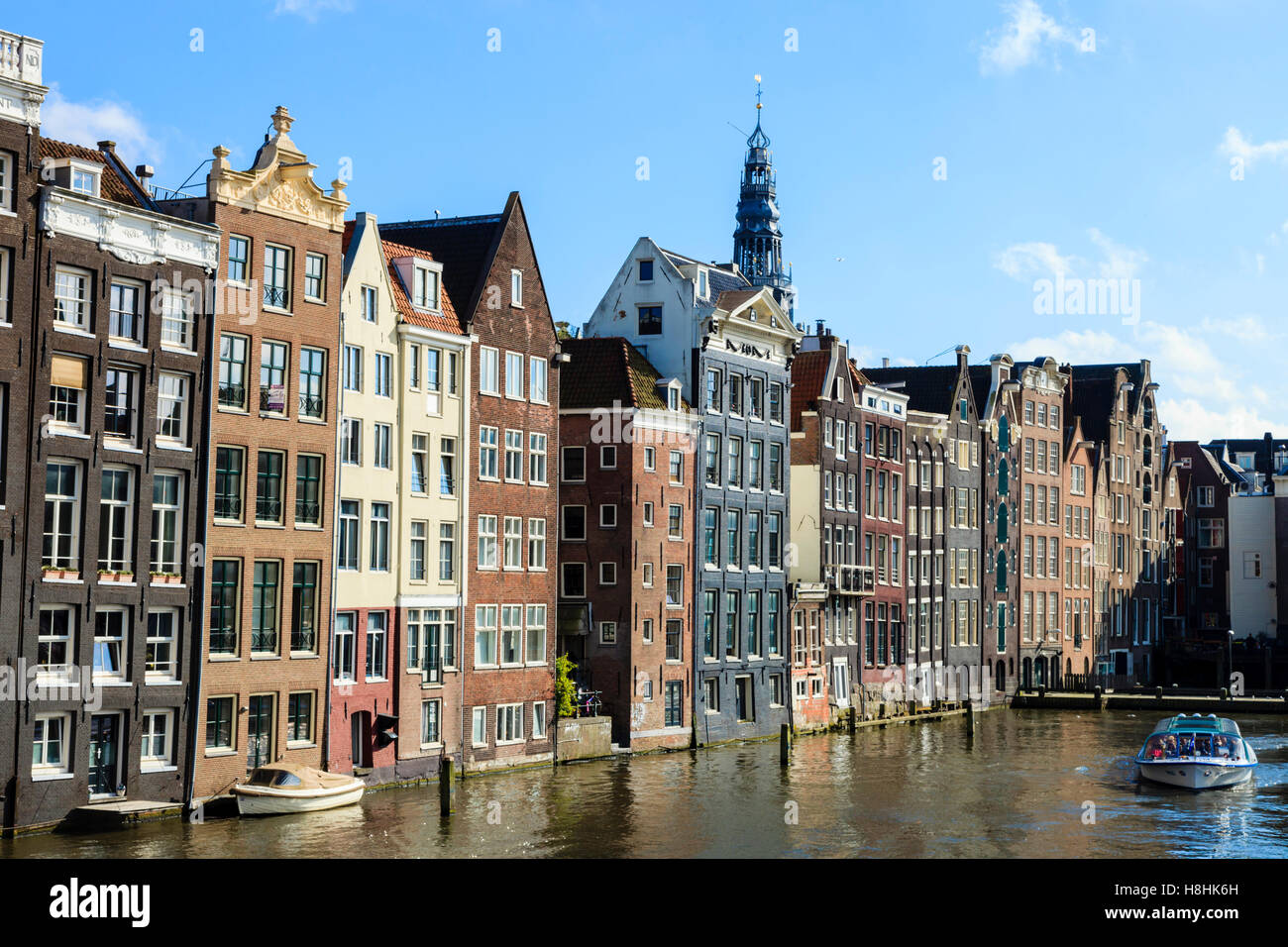 Ein Ausflugsboot Motoren zusammen vor der berühmten Häuser säumen den Rand der Damrak Canal Basin, Amsterdam, Niederlande Stockfoto