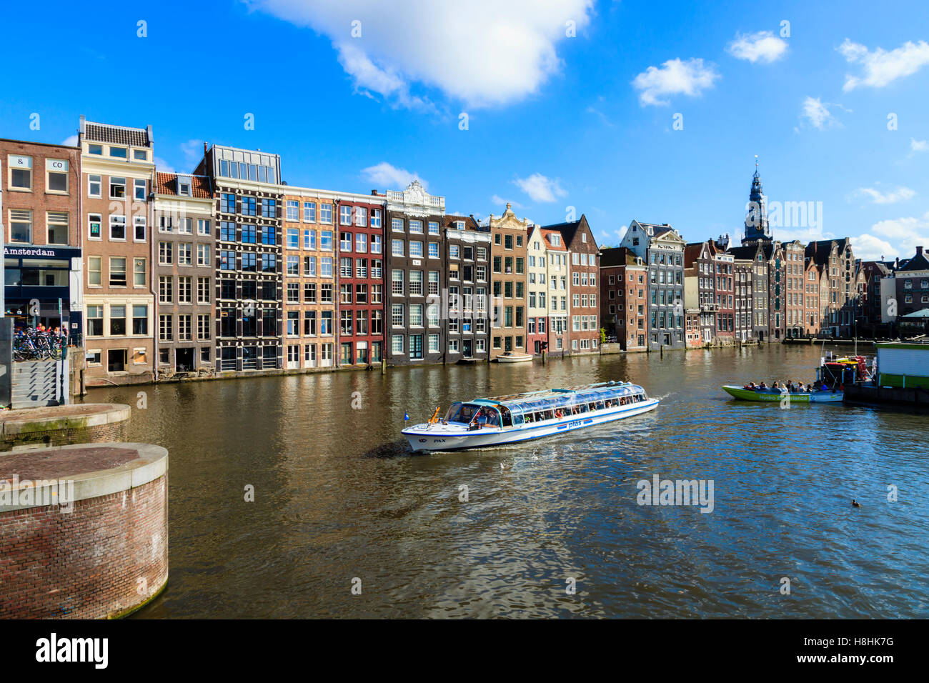 Ein Ausflugsboot Motoren zusammen vor der berühmten Häuser säumen den Rand der Damrak Canal Basin, Amsterdam, Niederlande Stockfoto