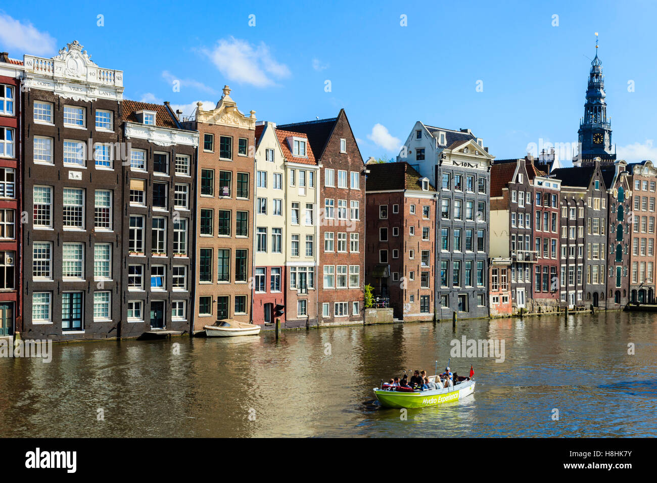Ein Ausflugsboot Motoren zusammen vor der berühmten Häuser säumen den Rand der Damrak Canal Basin, Amsterdam, Niederlande Stockfoto