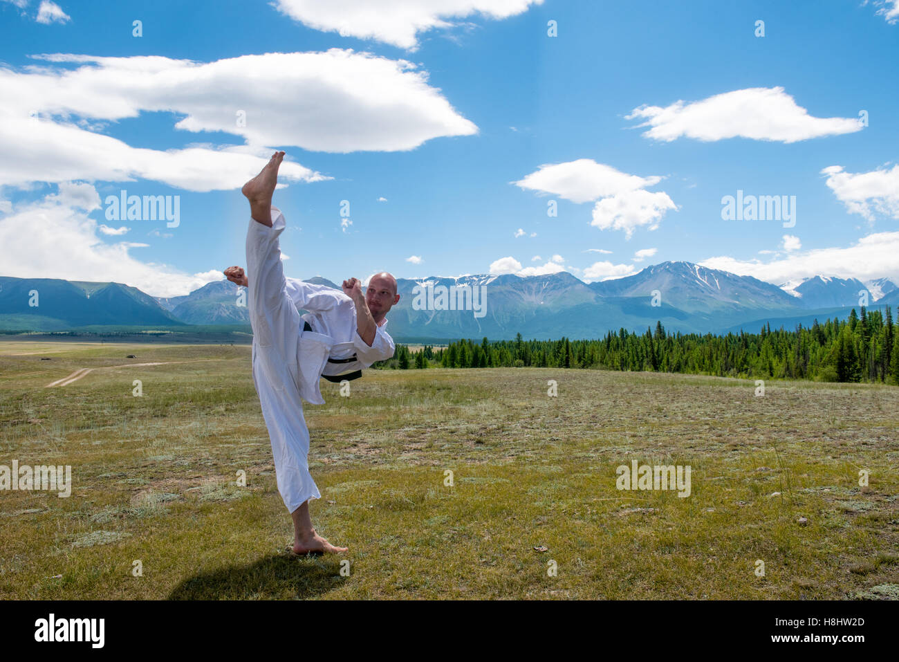 Mann in weißen Kimono und Black Belt Training Karate auf Gebirgshintergrund. Stockfoto