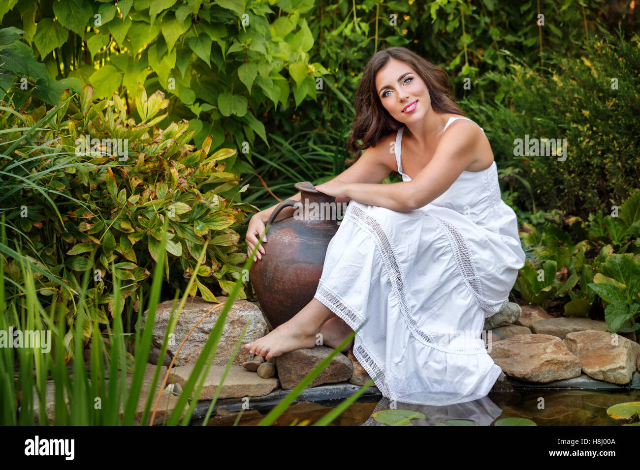 Hübsches junges Mädchen in einem weißen Kleid hält die alte Tonkrug sitzen am Teich mit Lilien. Stockfoto