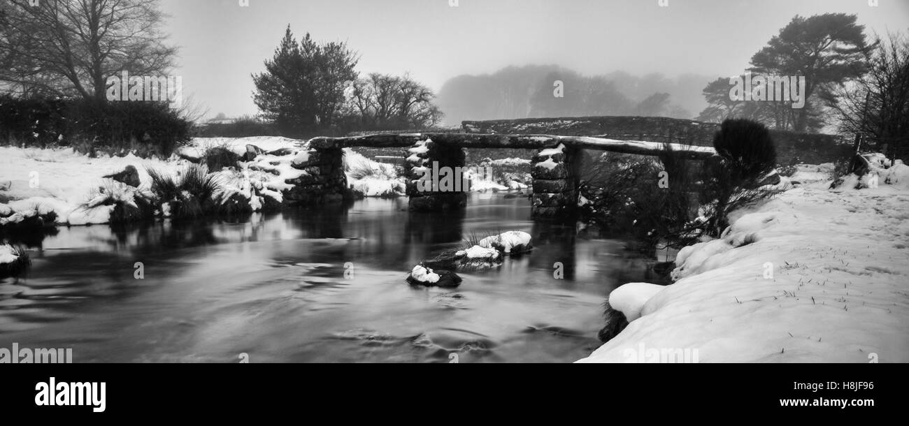Zwei Brücken auf Dartmoor im Winter mit einem nebligen Hintergrund und schneebedeckten Banken und ein eiskaltes East Dart River. Stockfoto
