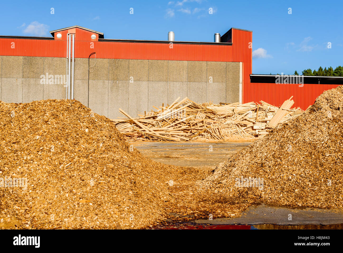 Hölzerne Trümmerhaufen vor roten Industriegebäude. Das Holz ist Abfall aus dem Sägewerk und zu Hackschnitzel erfolgt eine Stockfoto